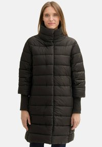 Crna, quilted puffer jakna s visokim ovratnikom, kratkim rukavima i ravnim krojem koji pada do sredine bedara. Glatka tekstura, minimalne metalne detalje.