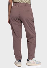 Braune, strukturierte, locker sitzende Outdoor-Hosen mit Gesäßtasche, kombiniert mit grauen und pastellfarbenen Sneakers. Verstellbares Taillendetail.