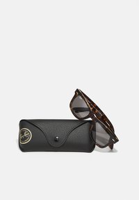 Lunettes de soleil en écaille de tortue avec des verres gris à côté d'un étui noir texturé avec un logo doré et une fermeture à pression. Marque de designer Ray-Ban.