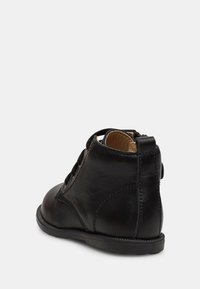 Botines de cuero negro con puntera redondeada, detalles de costura y una asa en la parte posterior. La suela es plana con un dibujo mínimo.