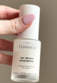Sérum facial de ácido hialurónico Flânerie Lily Bloom en un frasco de vidrio blanco mate con una tapa blanca. La etiqueta presenta texto en negro y certificación vegana.