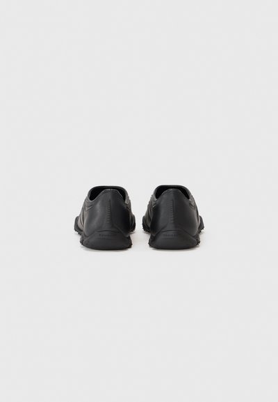 Zapatos de exterior minimalistas en negro con un acabado de cuero suave, diseño de perfil bajo y suelas de goma texturizadas. La vista trasera muestra un sutil logo.