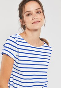 T-shirt rayé bleu et blanc avec un col rond et des manches retroussées. Fabriqué en tissu doux, avec des rayures horizontales régulières.