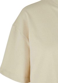 Camiseta de manga corta beige hecha de algodón suave, con un escote redondo, que presenta una textura lisa y detalles de costura simples.