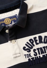 Marineblauwe en crèmekleurige gestreepte polo-shirt van katoen, met een knoopsluiting, geborduurd logo en een gecanneleerde kraag.