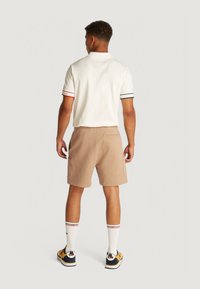 Polo bianco con accenti a righe sulle maniche, abbinato a pantaloni corti beige con tasche. Indossato con calze bianche e sneakers colorate.