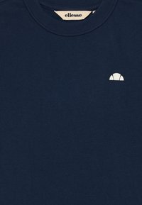 Mørkeblå T-skjorte med rund hals, liten hvit halvmåne-logo på venstre bryst, og "ellesse" merkeetikett inne i kragen.