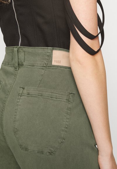 Calças verde escuras com uma textura suave, apresentando um remendo de couro rotulado "PAIGE" na parte de trás e um bolso traseiro com um contorno costurado.