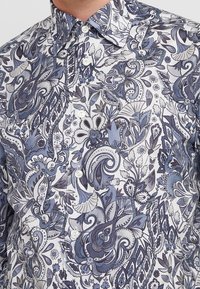 Męska koszula zapinana na guziki z gęstymi, skomplikowanymi niebieskimi i szarymi wzorami kwiatów oraz paisley na białym tle.
