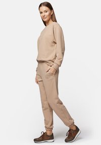 Beżowa bluza z okrągłym dekoltem i haftowanym napisem, w połączeniu ze spodniami dresowymi o dopasowanej kolorystyce z elastycznymi mankietami i bocznymi kieszeniami. Brązowe sneakersy na sznurówki.