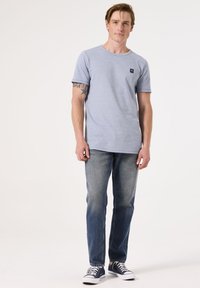 Camiseta de rayas gris de manga corta con cuello redondo y un pequeño logo, combinada con jeans azules y zapatillas de deporte en color marino.