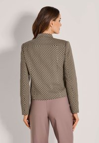 Textured blazer met een geometrisch patroon in beige en bruin. Kenmerken zijn lange mouwen, een cropped ontwerp en een hoge kraag. Gekozen in combinatie met lichtroze broeken.