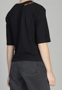 Camiseta de algodón negra con mangas cortas y un corte relajado. Cuenta con la frase "Tómate tu tiempo" bordada en naranja en la parte posterior del cuello.