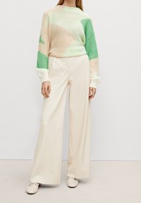 Suéter de punto en verde pastel y beige con patrones abstractos, combinado con pantalones anchos crema y zapatos beige con herrajes decorativos.