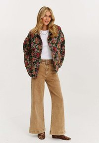 Bomberka w kwiatowy wzór, czarna i zielona, kremowa bluzka, beżowe spodnie z szerokimi nogawkami i buty w panterkę. Tkanina wydaje się być teksturowana.