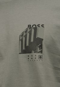 Κοντινό πλάνο ανοιχτόχρωμου γκρι υφάσματος με μαύρο γραφικό ενός κτιρίου και κείμενο «BOSS» και «OST OFF RECORDS» στην πρόσοψη.