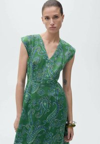Grünes Kleid mit V-Ausschnitt und kurzen Ärmeln, verziert mit einem blauen Paisleymuster. Glatter Stoff mit taillierter Passform.