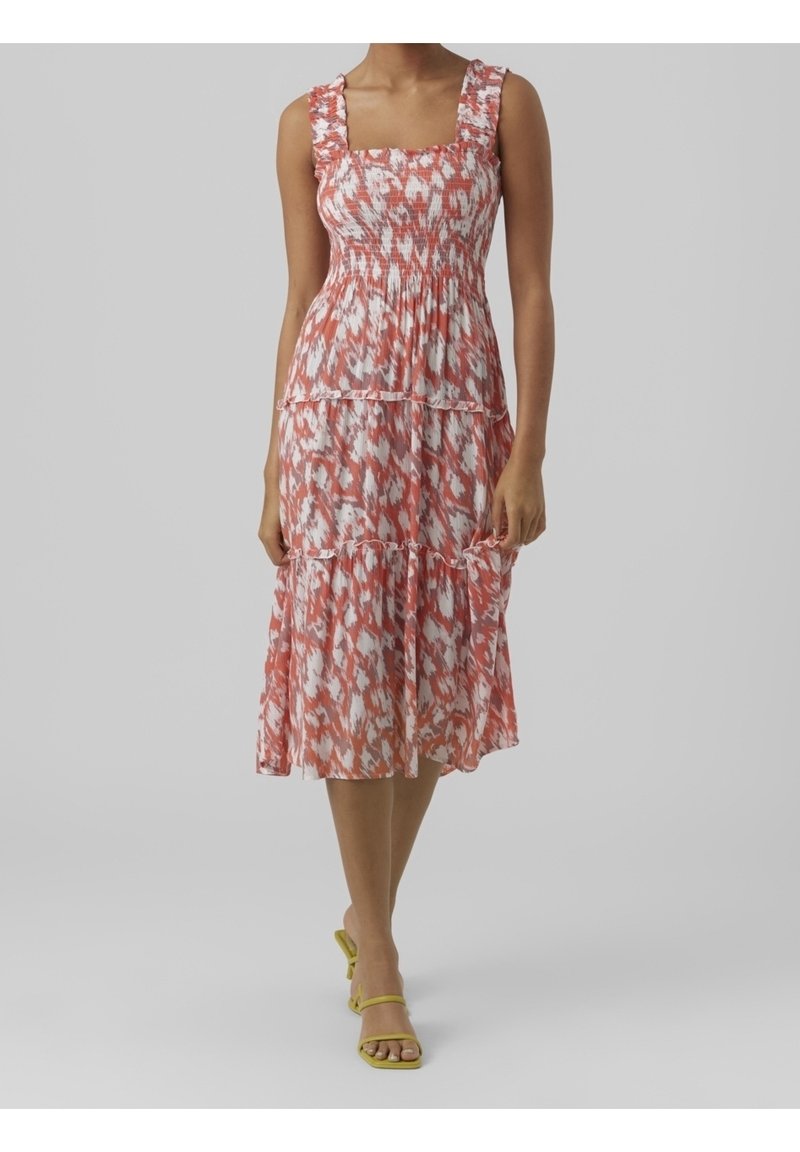 Robe midi avec un motif floral rose et blanc, présentant un buste plissé, une jupe à niveaux et des bretelles à volants. Associée à des talons jaunes.