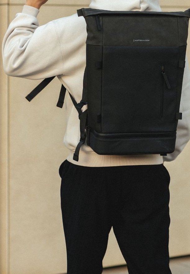 Musta rullatutti reppu, jossa on säädettävät olkahihnat, teksturoitu kangas, etutasku vetoketjulla ja logoyksityiskohtia yläosassa.