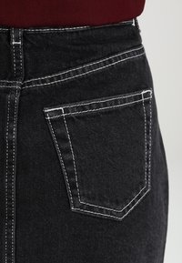 Svart denimkjol med vit söm, hög midja och en enkel bakficka, med en klassisk form och textur.