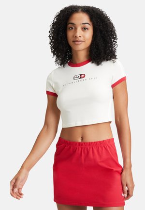 T-shirt blanc raccourci avec des bords rouges, arborant un logo noir, assorti d'une jupe courte en tissu élastique rouge. Tissu lisse, design décontracté.