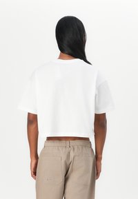 Hvit cropped t-skjorte med korte ermer, med en myk tekstur. Kombinert med beige bukser med elastisk midje og synlige baklommer.