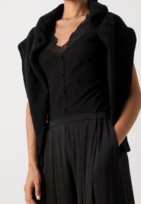 Černý žebrovaný top na ramínka s krajkovým lemem, doplněný černým pleteným šálou a plisovanou černou sukní, které vystihují hladké, plynulé textury.