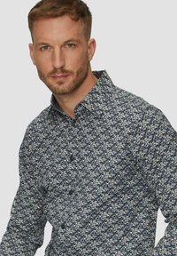 Marineblaues, gemustertes Hemd mit Knopfleiste, das ein geometrisches Design in Hellblau und Creme aufweist. Hergestellt aus einem glatten Stoff mit einem Standardkragen.