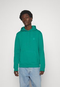 Turquoise hoodie with a kangaroo pocket, drawstring hood, and a small, square patch on the chest. Features ribbed cuffs and hem.