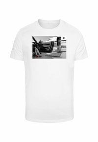 White t-shirt featuring a black-and-white print of a woman’s legs in red high heels next to a luxury car and private jet.