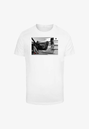 Witte t-shirt met een zwart-wit print van de benen van een vrouw in rode hoge hakken naast een luxe auto en privéjet.
