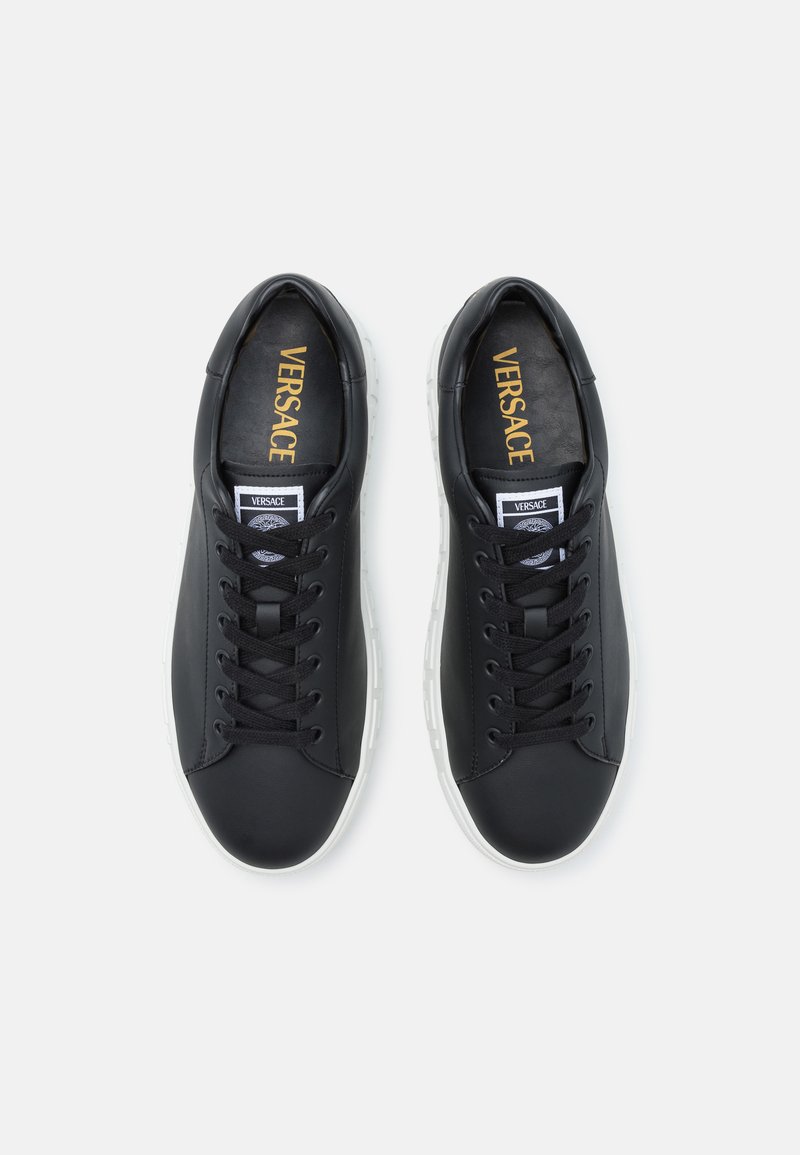 Baskets en cuir noir avec semelles en caoutchouc blanches, bout arrondi, lacets plats noirs et logo doré "Versace" sur les semelles intérieures.