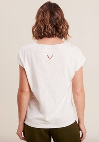 Weißes T-Shirt mit kurzen Ärmeln, das einen zarten bestickten Rücken mit Ausschnittdetails zeigt, gefertigt aus weichem, leichtem Stoff.