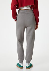 Grijze joggingbroek met een elastische tailleband en boorden, gecombineerd met groene sneakers. Het ontwerp is relaxed-fit en minimalistisch.