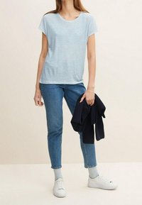 Bílý a světle modrý pruhovaný tričko s kulatým výstřihem, spárované s modrými džíny a bílými teniskami, drží tmavý cardigan.