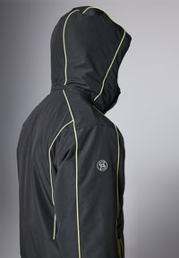 Chaqueta con capucha negra y costuras de contraste amarillas, que presenta un logo en la manga, fabricada con un material suave y duradero.