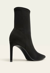 Mustat korkeat saappaat, joissa on sleek, sileä kangaspinta, terävä kärki ja hoikka stiletton korko. Nilkkamittainen muotoilu, jossa on huomaamattomat sauma-yksityiskohdat.