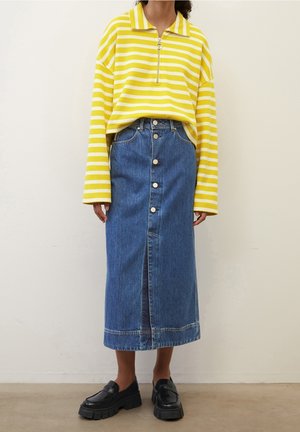 Žlutý a bílý pruhovaný top s dlouhým rukávem a zipem na krku, doplněný modrou džínovou sukní na knoflíky a černými masivními mokasínami.