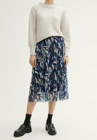 Maglione a coste grigio chiaro con collo alto, abbinato a una gonna fluida e patterned in navy con design floreali astratti in rosa e blu.