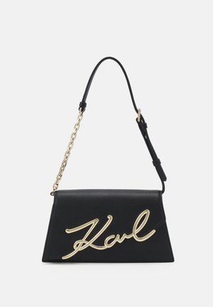 Sac à main en cuir noir au design structuré, avec un logo en or, une bandoulière en chaîne détachable et une forme élégante et pliante.