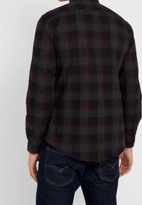 Camicia in flanella di colore grigio scuro con un motivo a quadri rosso e nero. Presenta maniche lunghe, polsini con bottone e orlo curvo. Design casual.