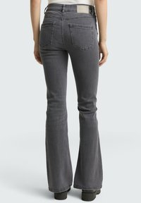 Jean flare gris avec un design classique à cinq poches, taille mi-haute et texture lisse. Présente un logo en patch à l'arrière.