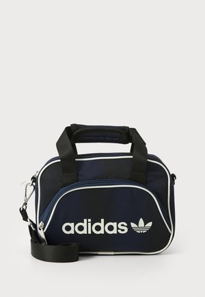 Bolsa de Adidas en azul marino con asas negras, acentos blancos y logo. Presenta un cierre con cremallera y una correa de hombro extraíble. Tela texturizada.