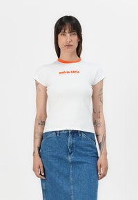 White short-sleeve t-shirt with an orange ribbed collar and the text "calvin klein" in orange, paired with a blue denim skirt.