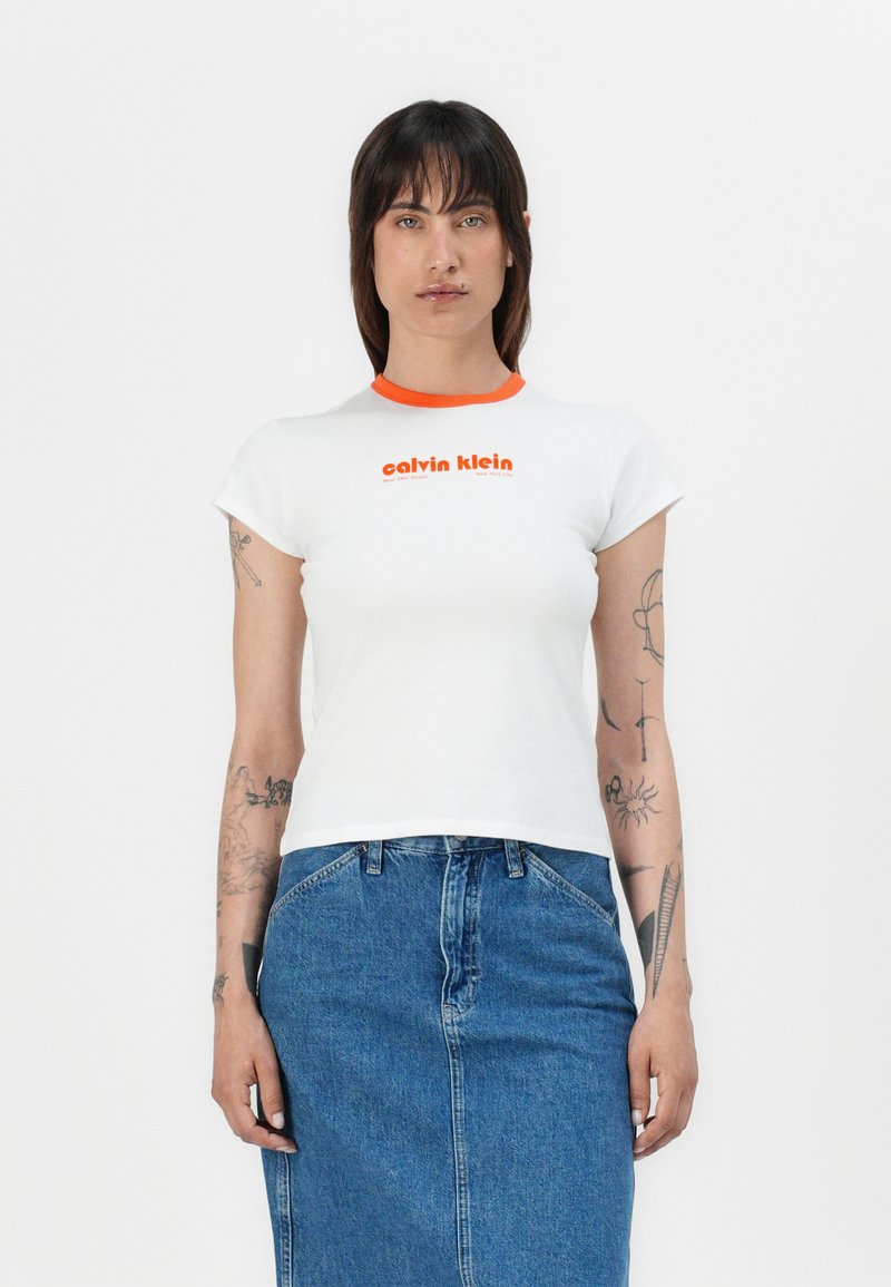 White short-sleeve t-shirt with an orange ribbed collar and the text "calvin klein" in orange, paired with a blue denim skirt.