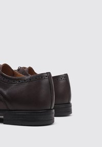 Zapatos de vestir de cuero marrón, con detalles de brogue, textura suave, forma redondeada y suela de goma negra.