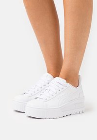 Vita plattformssneakers med en slät syntetisk ovandel, rund tå och tjock gummisula. Funktioner inkluderar snörning och logotyp på sidan.