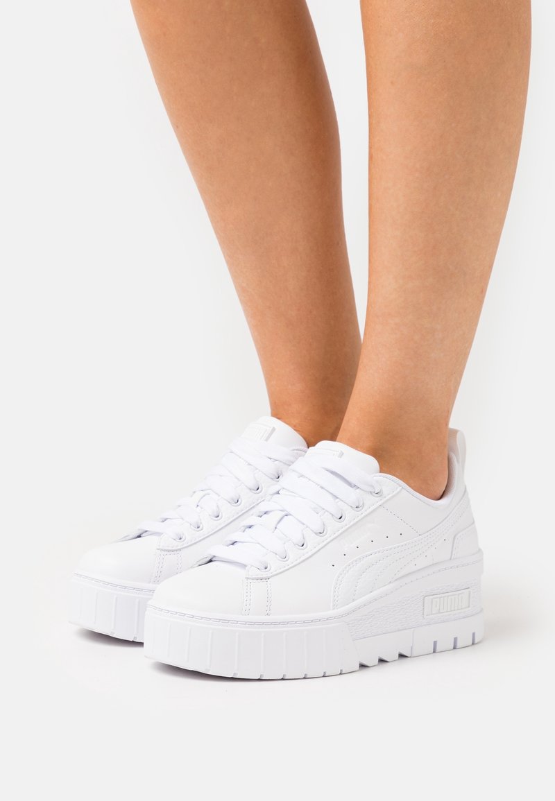 Vita plattformssneakers med en slät syntetisk ovandel, rund tå och tjock gummisula. Funktioner inkluderar snörning och logotyp på sidan.