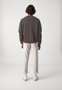 Mørkebrun sweatshirt med rund hals, afslappet pasform og ribbede manchetter; parret med lysebeige opstillede bukser og hvide sneakers.