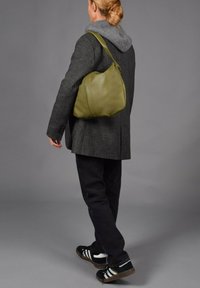 Olijfgroene leren schoudertas met een naadloos, gebogen ontwerp. Zachte textuur en minimale stiksels. Te dragen op de schouder met een verstelbare schouderband.